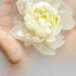 Therapies - Unrecognizable female with soft manicured hands holding white flower with delicate petals in hands during spa procedures