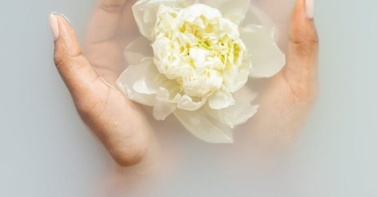 Therapies - Unrecognizable female with soft manicured hands holding white flower with delicate petals in hands during spa procedures
