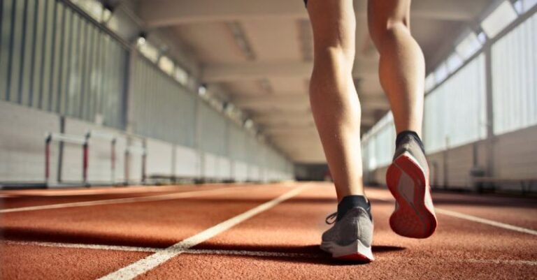 Physical Activity - From below back view of crop strong runner walking along running track in athletics arena while doing warm up exercises during workout