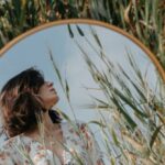 Self-Reflection - A woman in a field looking at a mirror