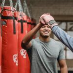 Personal Success - Positive ethnic male coach having high five with female after boxing training in gym with punching bags
