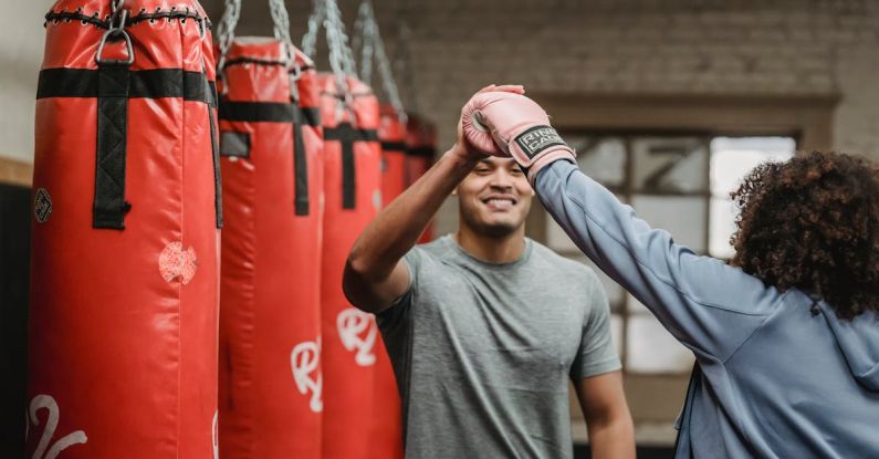 Personal Success - Positive ethnic male coach having high five with female after boxing training in gym with punching bags