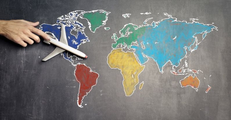 Global Citizenship - Top view of crop anonymous person holding toy airplane on colorful world map drawn on chalkboard